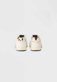 Hvide sneakers med en struktureret, blød overdel, der har brune accenter og legende mønstre bagpå. Gummisåler i en lys beige farve.