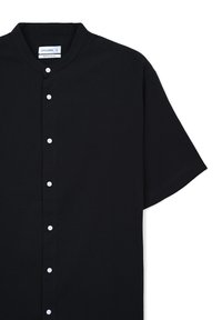 Chemise noire à manches courtes avec col mandarin, en tissu à texture lisse, ornée de boutons blancs sur le devant.