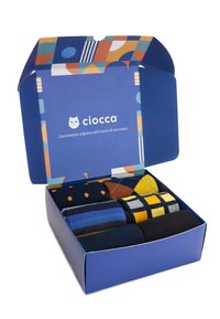 Set von sechs Socken in einer blauen Box mit einem geometrisch gemusterten Innenraum. Die Socken haben verschiedene Farben und Muster, einschließlich Streifen und Punkten.