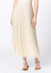 Ljus krämfärgad plisserad kjol i spets med blommönster, med en platt midja. Bärs med silversandaler.