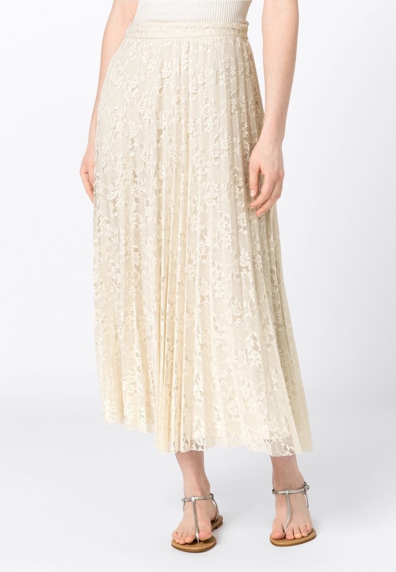 Ljus krämfärgad plisserad kjol i spets med blommönster, med en platt midja. Bärs med silversandaler.