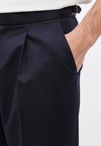 Καλοραμμένο παντελόνι σε ναυτικό μπλε χρώμα με λεία υφή, διαθέτει πτυχώσεις στο μπροστινό μέρος και τσέπες. Η ζώνη έχει θηλιές για ζώνη.