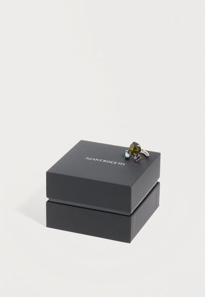 Κοσμηματοθήκη Black Man Crocetti με τρία πολύχρωμα δαχτυλίδια από πολύτιμους λίθους στην κορυφή, πάνω σε λευκό φόντο.