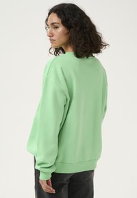 Sweatshirt surdimensionné vert clair avec des manches longues et des poignets côtelés, présentant un design simple et une texture douce. Vue arrière affichée.