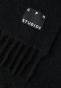 Czarny wełniany szalik z frędzlami, z prostokątną metką z napisem „CPH STUDIOS” białym tekstem na czarnym tle.