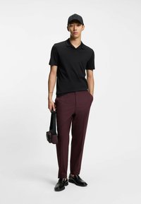 Polo negro, pantalones burdeos y zapatos negros. Los accesorios incluyen una bolsa pequeña con correa y una gorra negra. Texturas lisas, diseño ajustado.