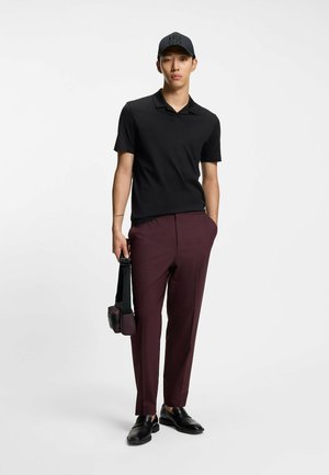 Svart pikétröja, bordeauxröda byxor och svarta skor. Accessoarer inkluderar en liten väska med axelrem och en svart keps. Släta texturer, figurnära design.