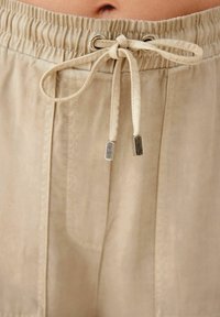 Beige træk-snor shorts lavet af et blødt, struktureret stof med elastisk talje, metal-spidse snore og sidelommer.
