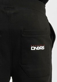 Pantaloni da tuta neri con vita a coste, dotati di due tasche laterali e logo "DANGEROUS" rosso e bianco sulla tasca destra. Materiale in misto cotone.