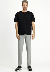 T-shirt nera a maniche corte abbinata a pantaloni slim-fit grigio chiaro. I pantaloni presentano una texture liscia; indossati con scarpe da ginnastica nere.
