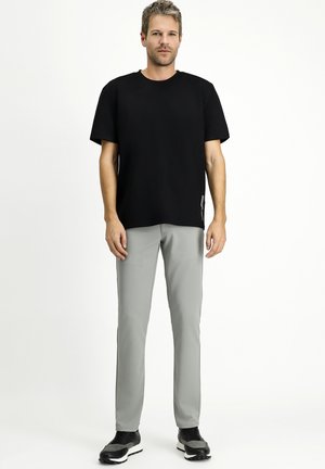 Camiseta negra de manga corta combinada con pantalones ajustados de color gris claro. Los pantalones tienen una textura suave; se llevan con zapatos deportivos negros.