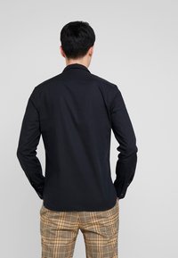 Heren zwart overhemd met lange mouwen, een kraag, manchetten met knopen en een gladde textuur, gecombineerd met geruite beige en bruine broek.