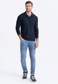 Marinblå långärmad polo med rak passform, i kombination med ljusblå slim fit-jeans och marinblå sneakers med vita sulor och snören.