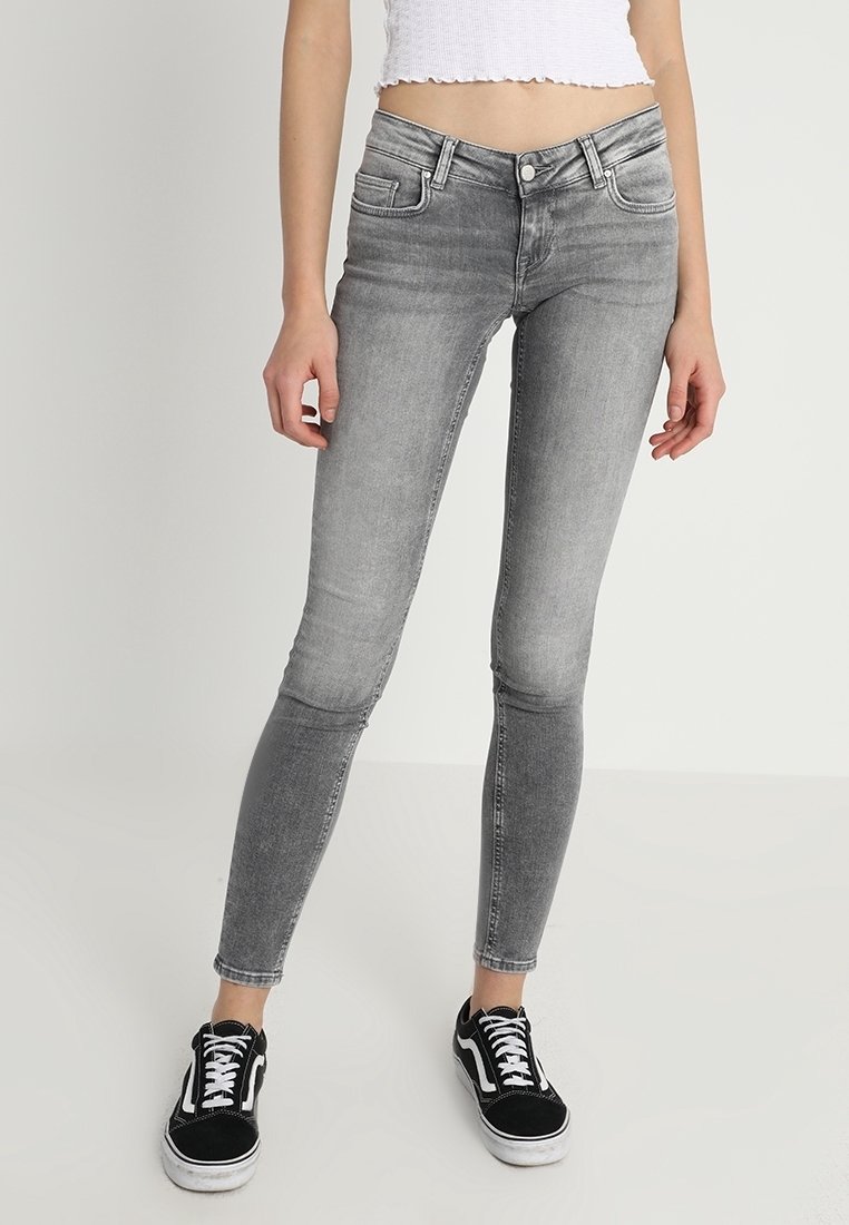 Pantalones vaqueros ajustados grises con una textura suave y un diseño clásico de cinco bolsillos, combinados con zapatillas negras con cordones blancos.