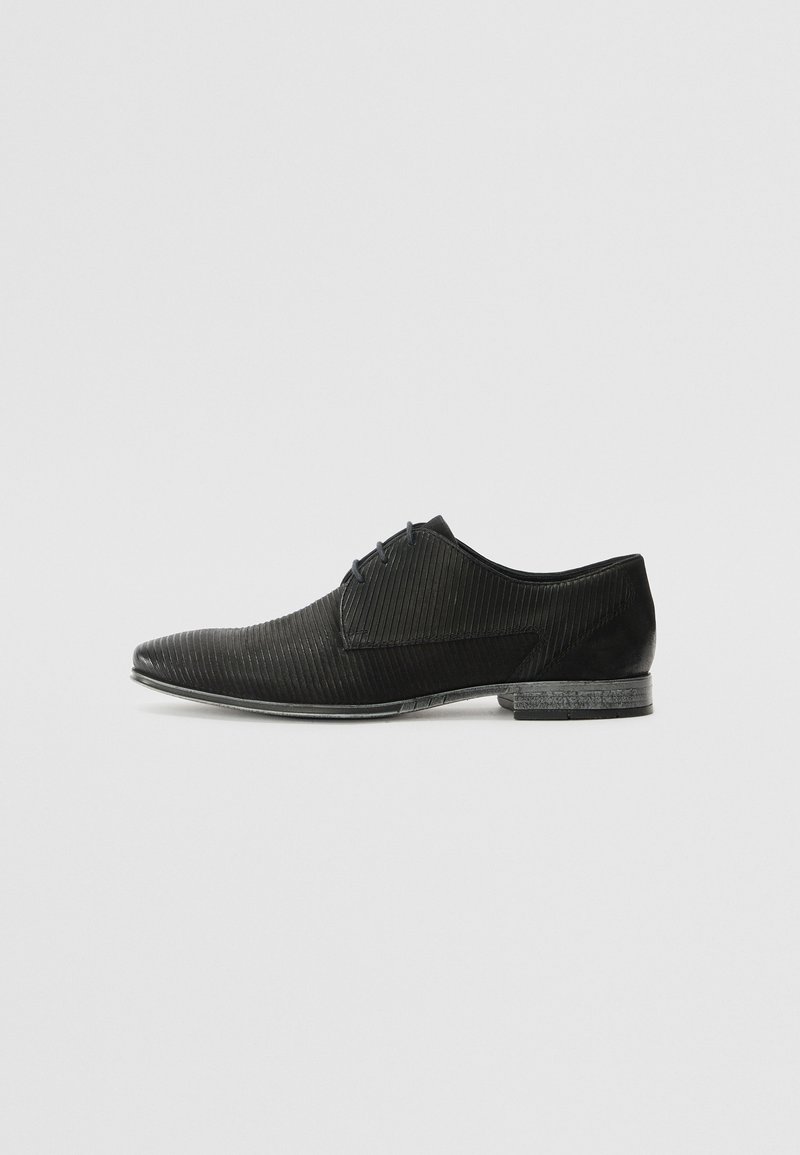 Chaussure noire à bout pointu, présentant une texture striée, des accents lisses et un talon bas. Le design est élégant et moderne.