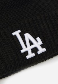 Fekete kötött sapka bordás textúrával és fehér hímzett "LA" logóval. Egyszerű dizájn, amely alkalmas különféle laza öltözetekhez.