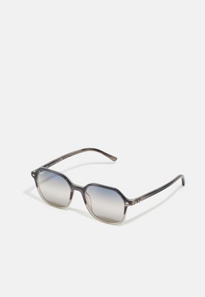 Óculos de sol com uma estrutura leve, em gradiente cinza, de formato octagonal e lentes escuras. Apresenta uma marcação discreta nas hastes.