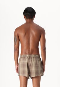 Brown and beige plaid boxers with an elastic waistband, displayed on a bare torso from a rear view, showcasing fabric texture and pattern.