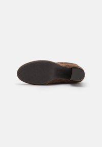 Bottines en suède marron avec une tige en tissu texturé et une semelle en caoutchouc, dotées d'un talon lisse et d'un motif de grip circulaire sur la semelle extérieure.