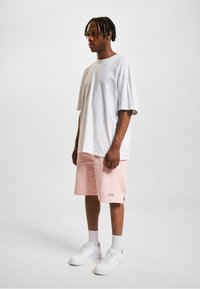 T-shirt oversize blanche, shorts roses avec logo, et baskets blanches. Texture lisse, coupe décontractée, shorts longueur genoux.