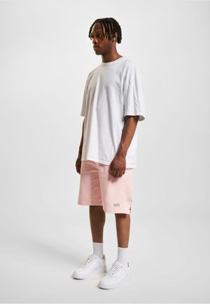 Hvid oversized t-shirt, lyserøde shorts med logo og hvide sneakers. Glat tekstur, afslappet pasform, knælange shorts.