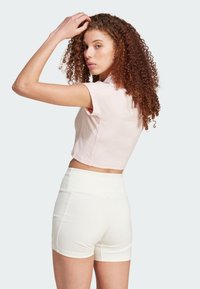 Light pink cropped top with short sleeves paired with high-waisted white ribbed shorts. Model shown turning with curly hair.
