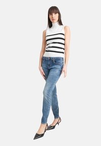 Witte mouwloze coltrui met zwarte strepen, gecombineerd met blauwe skinny jeans en zwarte puntige hakken. Eenvoudig en aangesloten ontwerp.