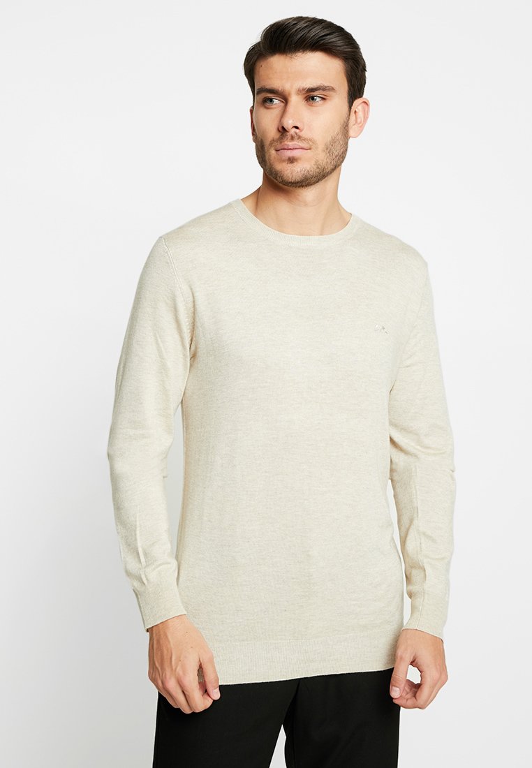 Beiger Strickpullover mit langen Ärmeln, Rundhalsausschnitt und subtiler Textur. Besitzt ein kleines Logo auf der Brust sowie gerippte Bündchen und Saum.