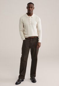 Polo à manches longues de texture crème avec fermeture à boutons, associé à un pantalon marron foncé et des mocassins noirs. Design simple et décontracté.