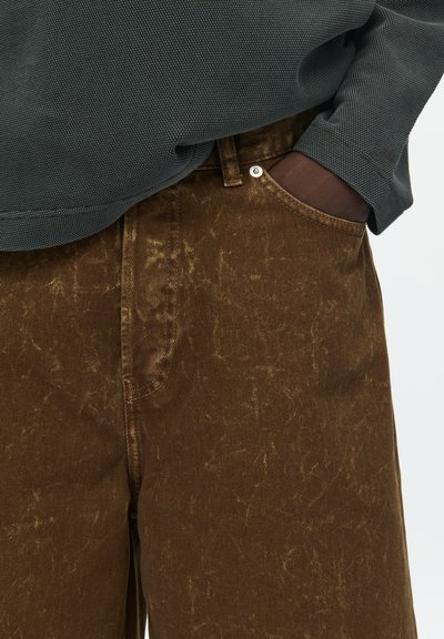 Brown denim pants with a textured finish, featuring a front pocket and a visible button. Paired with a dark grey, textured top.