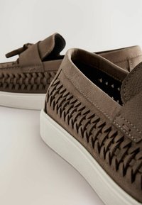 Brown leather shoes with woven pattern on sides, featuring a flat white rubber sole and a smooth, rounded toe.