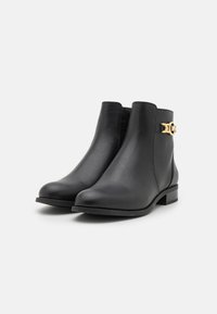 Bottines en cuir noir avec surface texturée, détail de boucle sur le côté en or, bout rond et petit talon en bloc. Design classique et minimaliste.