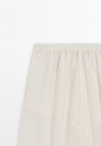Off-white tylskørt med elastik i taljen og et lagdelt, semi-gennemsigtigt stofdesign.