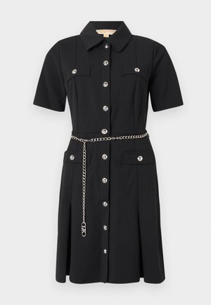 Zwarte, korte mouw jurk met zilveren knopen, klepzakken op borst en heupen, en een zilveren kettingriem, kraag en plooien aan de voorkant.