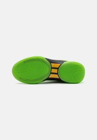 Zwarte sportschoen zool met helder groene rubber. Heeft cirkelvormige profielpatronen en een centrale gele accentstreep. Glad oppervlak.
