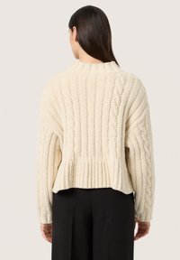 Cremefarvet kabelstrikket sweater med ribbet kant og sænkede skuldre, lavet af tekstureret stof. Kort længde med lange ærmer.