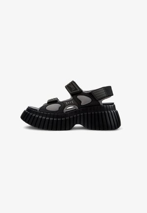 Sandales à plateforme noires et grises avec un bout ouvert, des sangles Velcro et une semelle striée. La partie supérieure présente des découpes pour la ventilation.