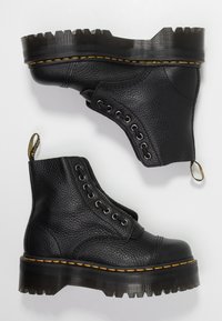 Bottines noires en cuir avec une finition texturée, des coutures jaunes et une semelle à chevauchement robuste. Comprend des œillets en métal et une languette.
