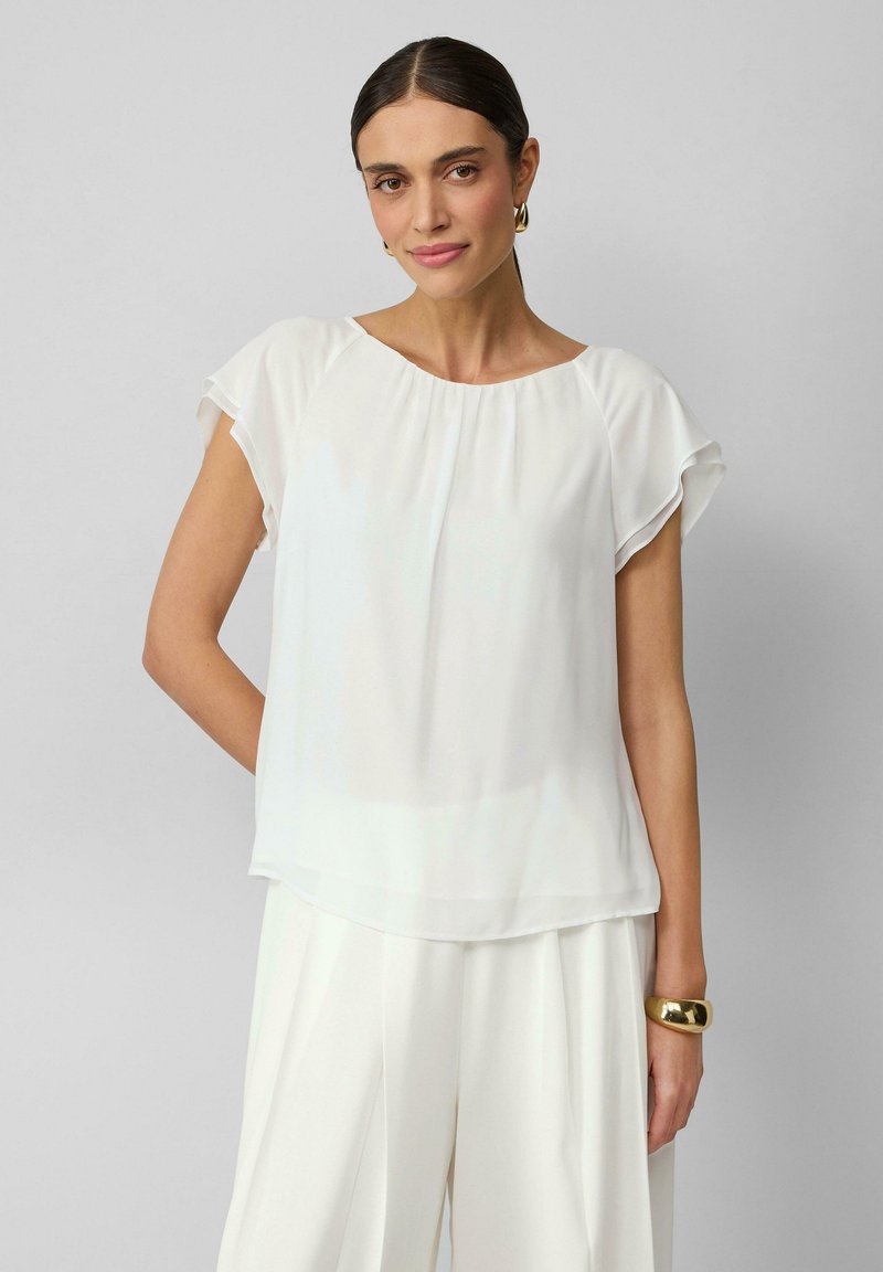 Witte lichtgewicht blouse met korte geplooide mouwen, ronde halslijn en vloeiende uitstraling. Draag het met hoge witte broek en een gouden armband.