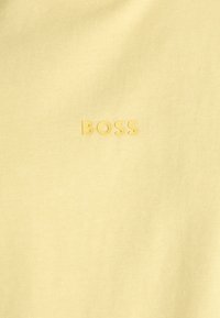 Svetlo žlté bavlnené tričko s jemnou textúrou a vystúpeným, embosovaným logom "BOSS" v rovnaké farbe na prednej strane.
