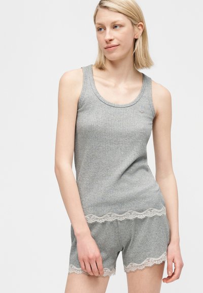 Ξανθιά γυναίκα που φοράει γκρι ριμπ τοπ χωρίς μανίκια και ταιριαστό σορτς με λευκή δαντέλα, στέκεται μπροστά σε έναν απλό ανοιχτόχρωμο φόντο.