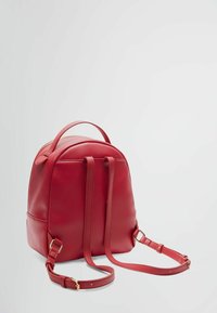 Zaino in pelle rossa con forma arrotondata, spallacci regolabili, chiusura con zip e una piccola maniglia superiore. Texture liscia con accenti in metallo dorato.