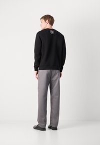 Sweatshirt preto com decote redondo e logótipo nas costas, emparelhado com calças cinzentas de perna reta e sapatos pretos. Textura de tecido suave.