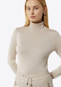Helles beige Rollkragensweatshirt aus weichem, geripptem Strick. Es hat lange Ärmel und eine figurbetonte Silhouette, kombiniert mit lockeren beigen Hosen.