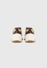 Brune og creme sneakers med en tekstureret overdel, chunky hvide såler og gummidetaljer. Har en flad hæl og et minimalistisk design.
