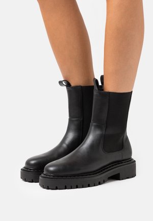 Czarne skórzane botki za kostkę z elastycznymi panelami po bokach, grubą podeszwą i dwoma pętelkami u góry ułatwiającymi zakładanie. Teksturowane wykończenie.