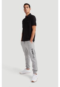 Black polo shirt with short sleeves, paired with gray sweatpants featuring a printed logo. White sneakers with orange accents.