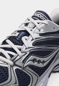 Κοντινό πλάνο σε ναυτικού μπλε και ασημί παπούτσι τρεξίματος Saucony με λευκά κορδόνια και αναπνεύσιμο ύφασμα από δίχτυ.