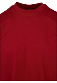 Tricou roșu din bumbac, cu guler rotund, mâneci scurte și o textură netedă și uniformă. Fără modele sau detalii suplimentare vizibile.