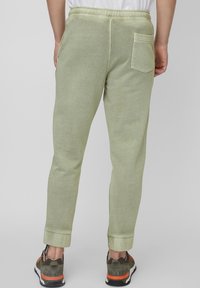 Ljusgröna joggingbyxor med uppvikta kanter, elastisk midja och en bakficka. Bärs med mörka sneakers med orangea accenter.